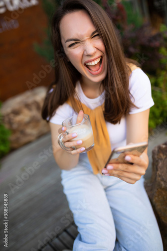 young charming girl makes a selfie on the phone while sitting in a summer green park