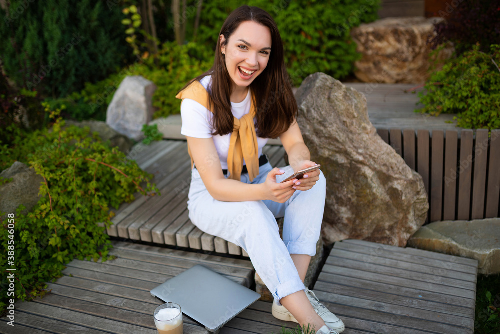 freelancer young woman communicates with clients on the phone while sitting in a green park freelancer young woman communicates with clients on the phone while sitting in a green park