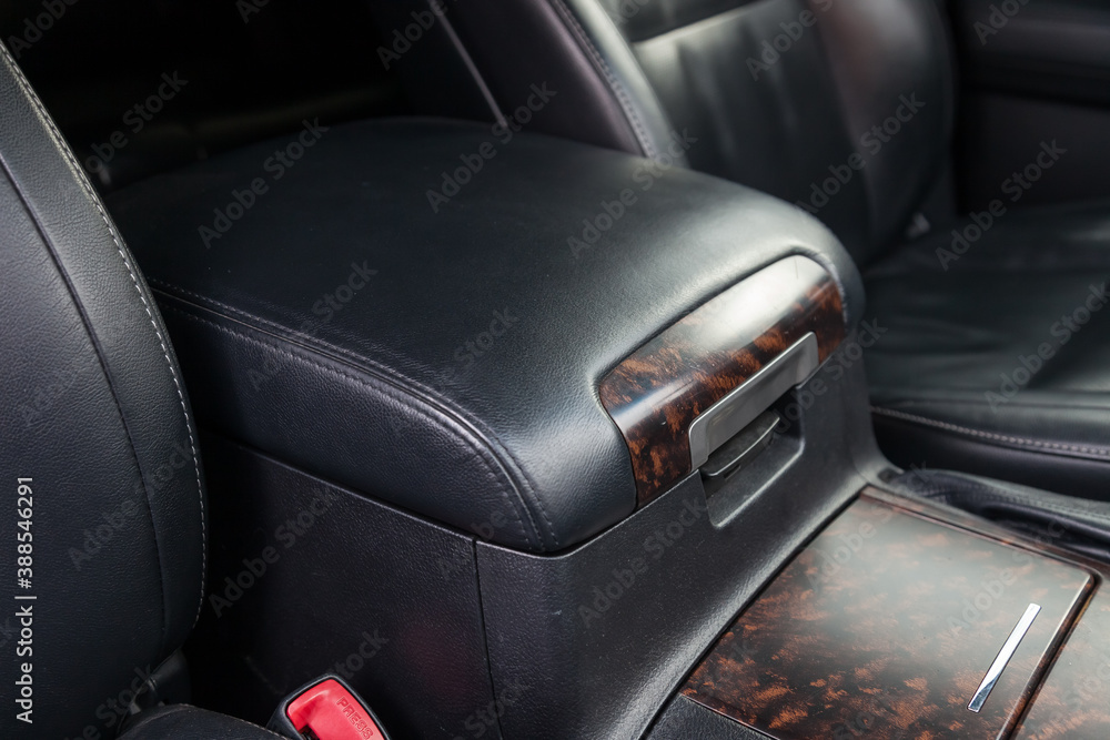Close-up of the armrest between the front seats in the car's interior on a wood-like panel covered in black leather. Glove box for storing small items.