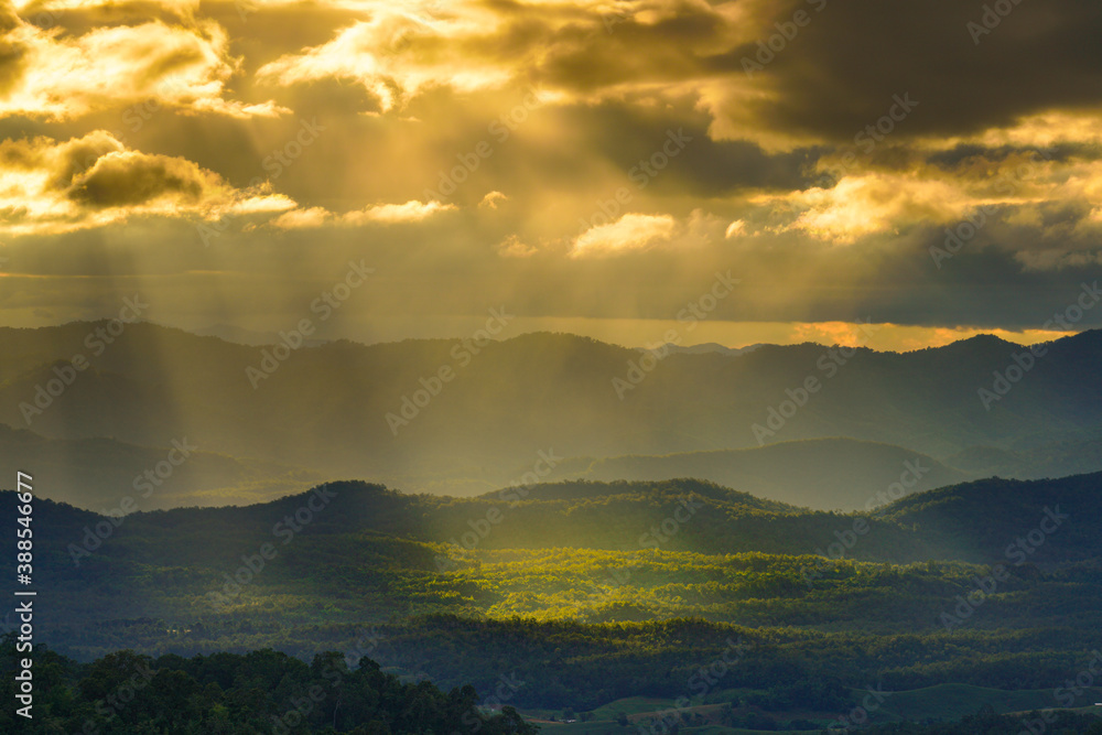 Yellow sun shafts through cloudy sky with long mountain range  and brighten foreest in Tak, Thailand