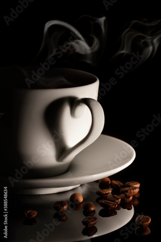 Cup of hot coffee with smoke and coffee beans on black background. A shadow in the shape of a heart.