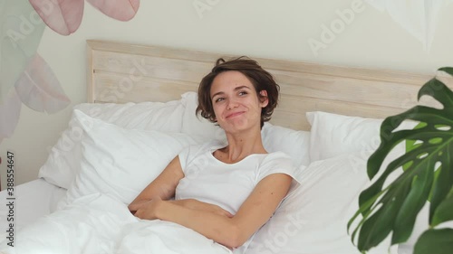 Pretty dreamful pensive calm young woman 20s yeras old in white t-shirt pajamas home wear lying in bed with white sheet pillow blanket spending time in bedroom. Rest relax good mood lifestyle concept photo