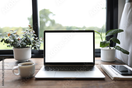 laptop mock up white blank screen with phone and coffee cup and plant pot on wooden table in front of windows 
