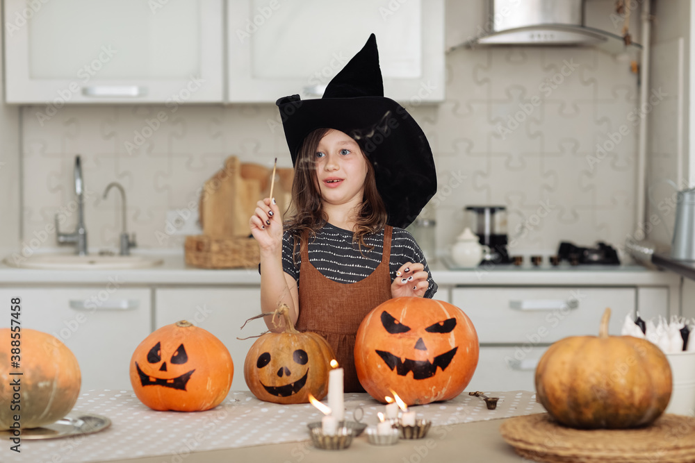 Fototapeta premium Happy halloween. Cute little girl in witch costume with carving pumpkin. Happy family preparing for Halloween. girl lights candles
