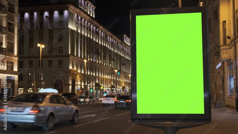 A green screen billboard located on the sidewalk on which people walk, next to a busy street. Cars move in the evening. 4K A green screen billboard located on the sidewalk on which people walk, next to a busy street. Cars move in the evening. 4K