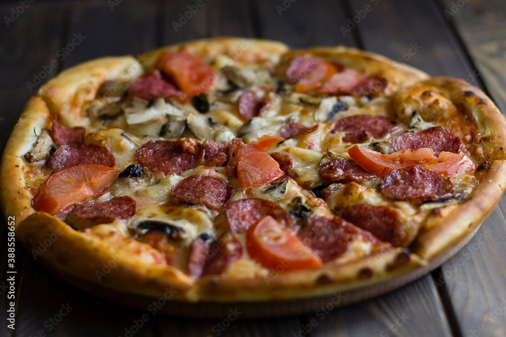 pizza with sausages, tomatoes and herbs, on a wooden background