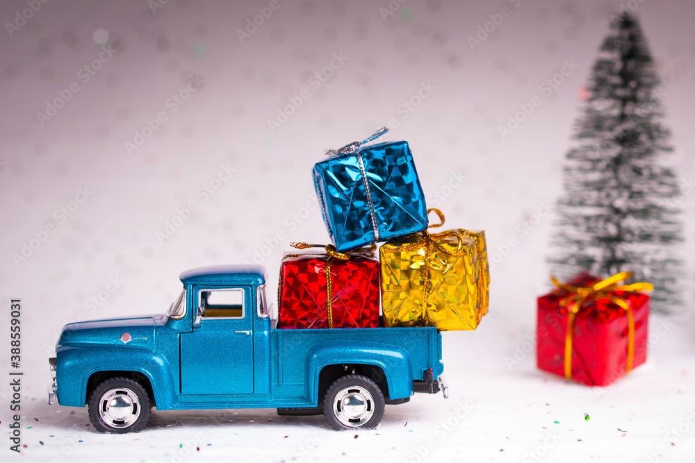 Santa pickup truck loaded with presents or gift. Box wrapped colored in sparkle paper. Christmas fir trees on the white snow background.