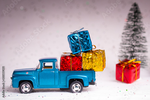 Santa pickup truck loaded with presents or gift. Box wrapped colored in sparkle paper. Christmas fir trees on the white snow background. © artiom.photo
