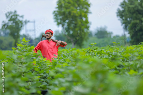 Young indian farmer holding farm equipment in hand at cotton field photo