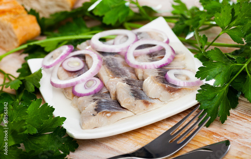 Delicious salted herring with onion and parsley on white plate