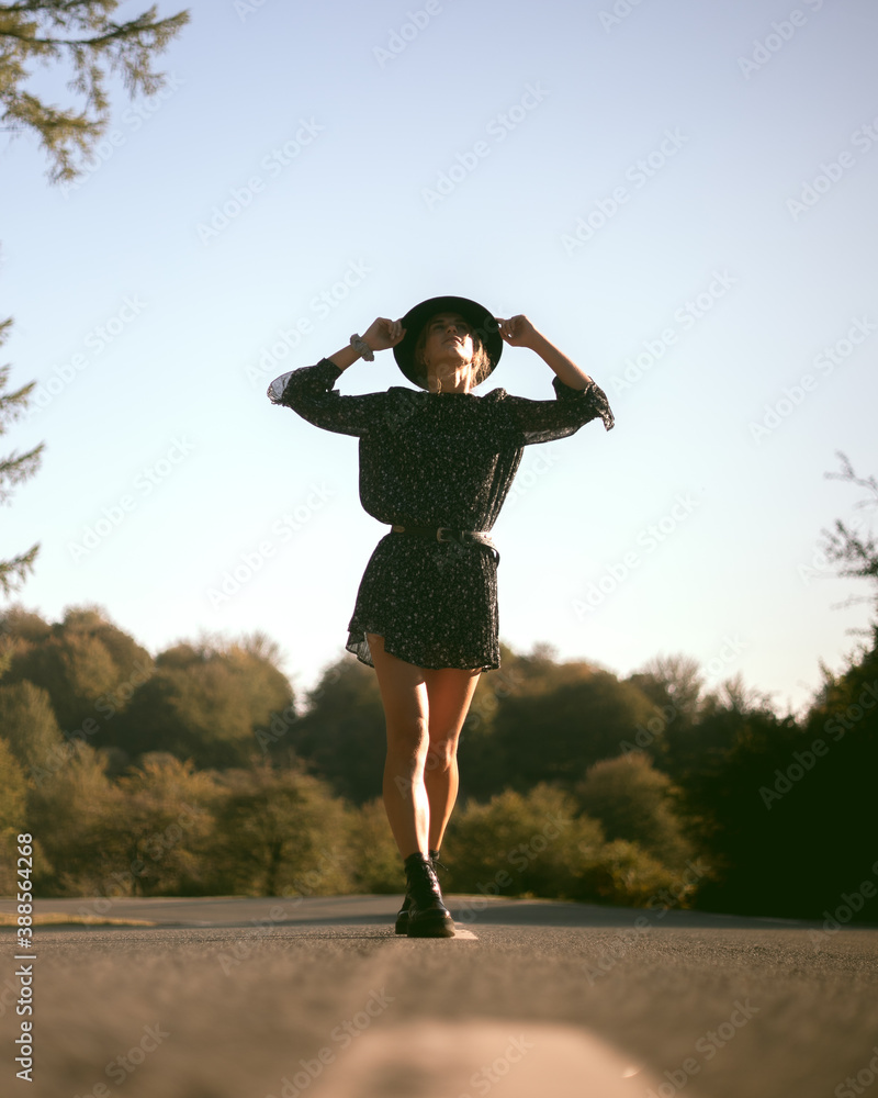 Trendy girl in the woods wearing a black dress and a fedora hat during autumn in Spain.