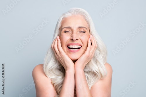 Close-up portrait of her she nice attractive excited cheerful grey-haired elderly lady touching cheeks laughing isolated gray pastel color background photo