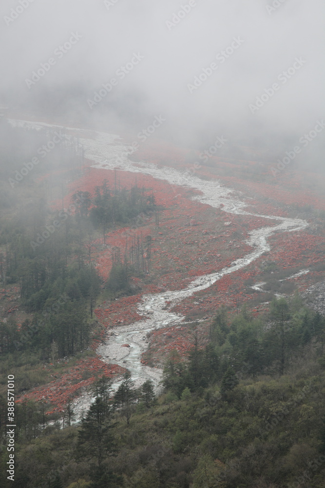 View of Red stone beach (Chinese: Hongshitan) with river under misty fog at Hailuogou Glacier Park in Garze Tibetan Autonomous Prefecture, Sichuan, China. The red color is the color of alga on rock.