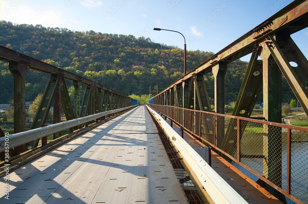 Obraz premium Rusty steel bridge across Dniester river in small village and mountains around. Ukraine.