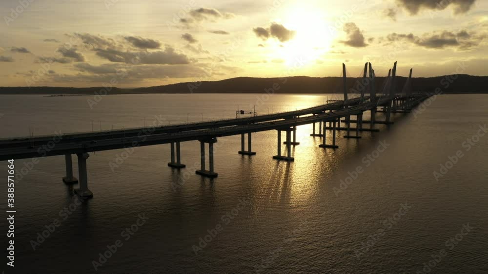 An aerial shot of the Mario M. Cuomo Bridge from the north side. The drone camera dolly out from the bridge over the Hudson River during a beautiful sunset. The bridge's shadow is on the river. An aerial shot of the Mario M. Cuomo Bridge from the north side. The drone camera dolly out from the bridge over the Hudson River during a beautiful sunset. The bridge's shadow is on the river.
