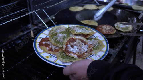 Plate being filled with freshly made traditional mexican dish chalupas with red and green salsa, onion and pork meat photo