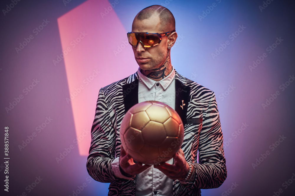 Plakat Styled and futuristic guy with eyewears poses with golden soccer ball in abstract background.