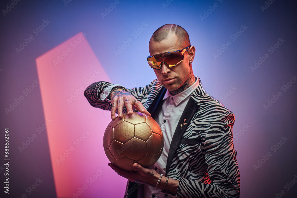 Plakat Futuristic man in suit with short haircut and eyewears poses with golden ball in colored abstract background.