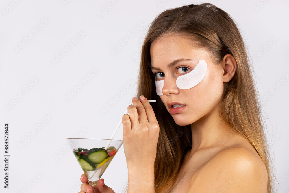 Portrait of a beautiful, young girl with long hair and eye patches and a cocktail in her hands. Skin care and healthy food concept. Photo on white background Portrait of a beautiful, young girl with long hair and eye patches and a cocktail in her hands. Skin care and healthy food concept. Photo on white background