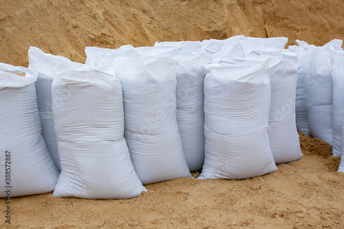 white sandbags stand in a row against a background of sand. building material in the package.