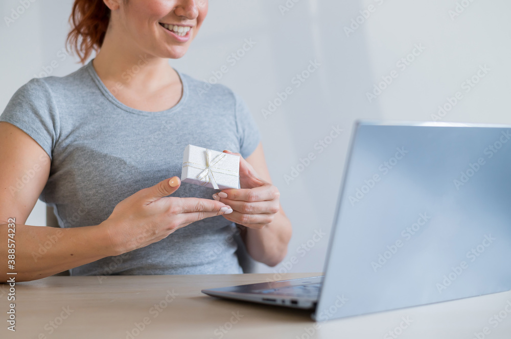 Online sale of gifts. A woman is holding a gift box in front of a laptop Online sale of gifts. A woman is holding a gift box in front of a laptop