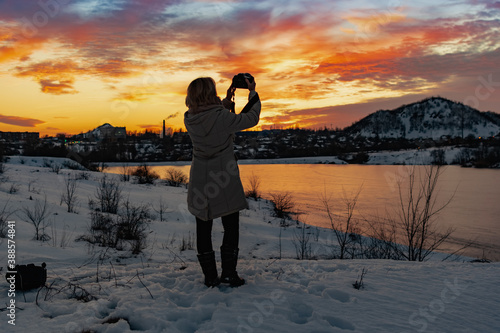 A girl with a camera shoots a colorful evening sunset on a cloudy sky from a height , the silhouette of the photographer in the darkened lighting in the open air with a beautiful view of the glow