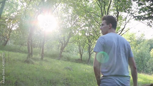 A man walks on a footpath in forest, daytime,  summer season. Young man filmed from behind while Walking Along Summer Forest Path.