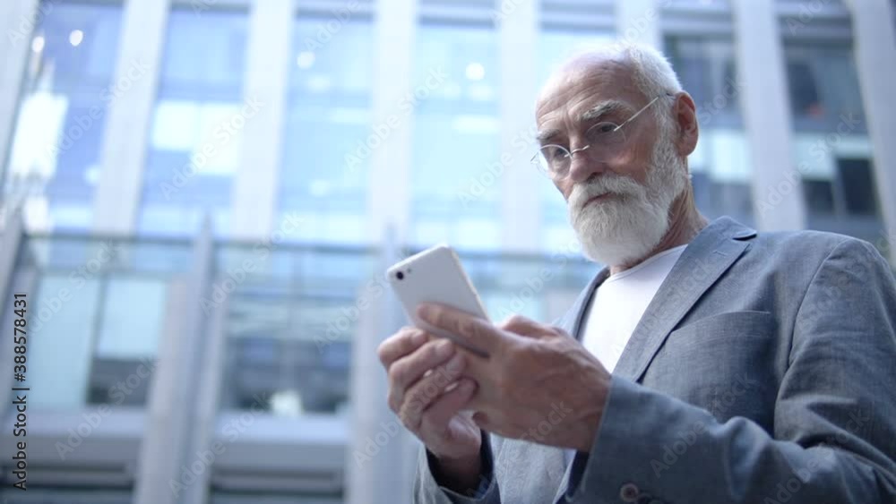 Mature businessman in eyeglasses typing email by smartphone application, blog Mature businessman in eyeglasses typing email by smartphone application, blog