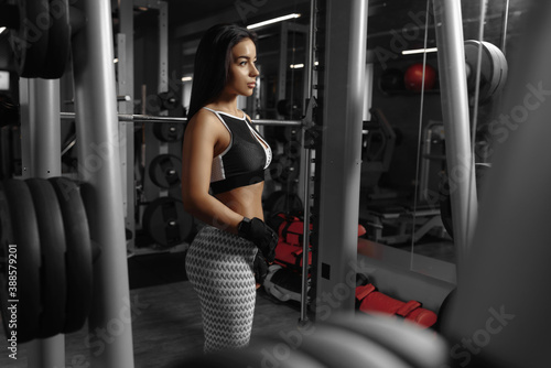 Serious hot fitness woman with perfect body poses in the gym looking to one side. Beautiful athletic girl, shaped abdominal. Fitness and sports concept