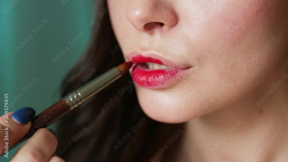 Makeup artist's hand with thin brush smears lipstick on model lips Makeup artist's hand with thin brush smears lipstick on model lips