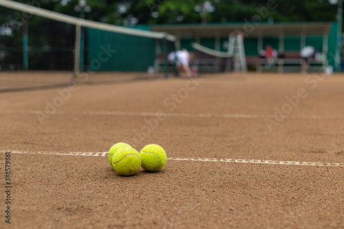 Three tennis balls lie together on a red clay court.