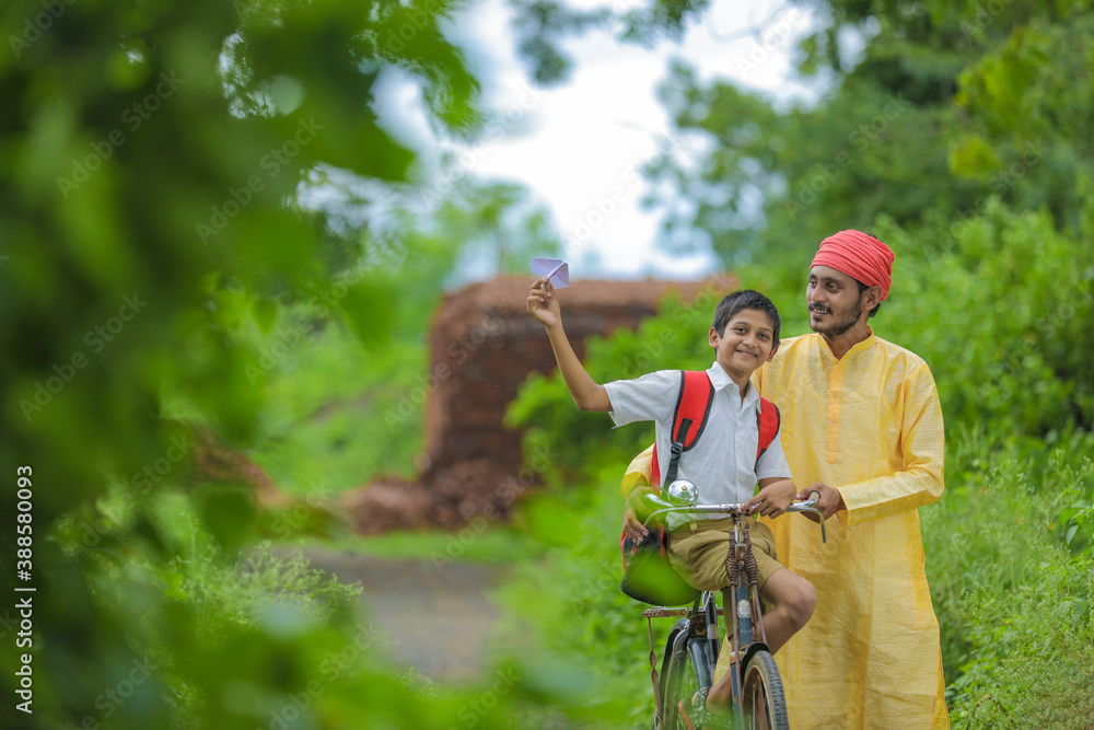 Obraz premium Young indian farmer and his son going to school on cycle