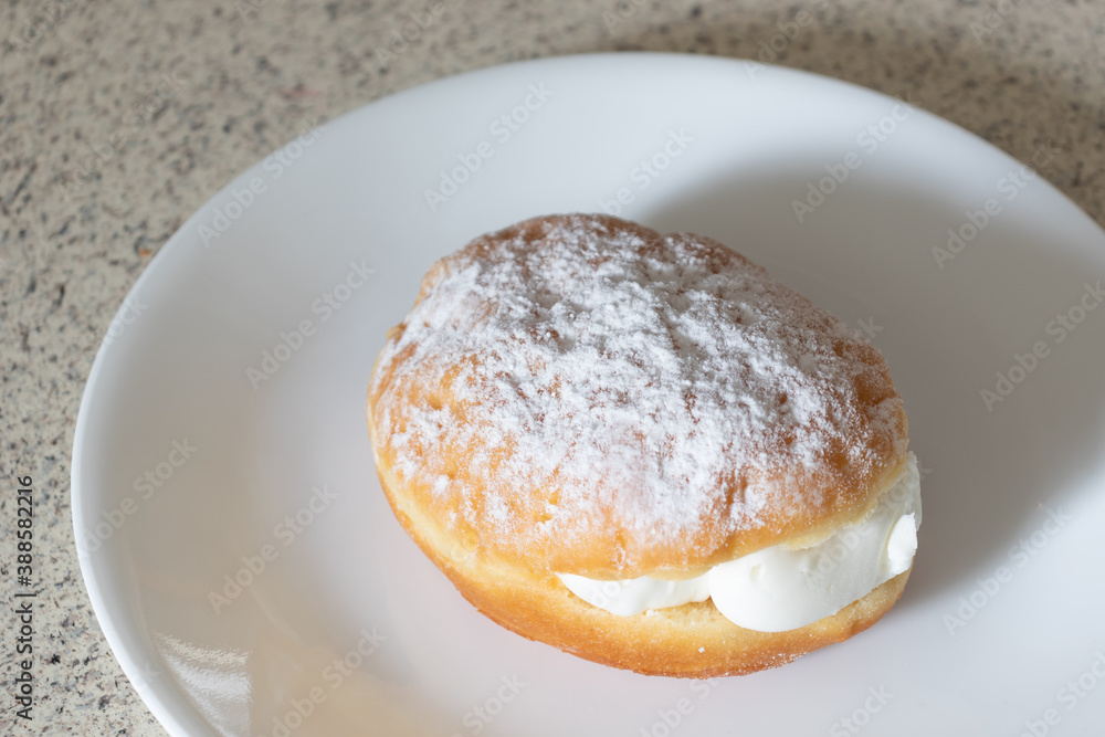 A powdered vanilla cream filled donut on a white plate waiting to be served.