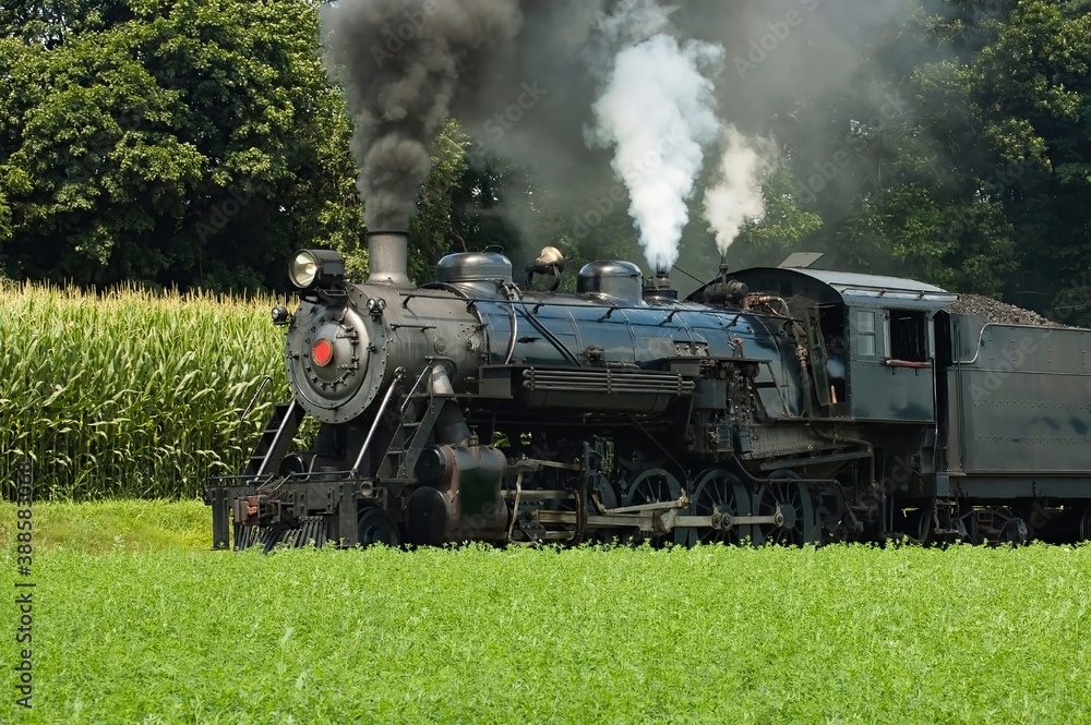 Obraz premium Close Up of an Antique Steam Passenger Train Puffing along Amish Countryside with Green Fields