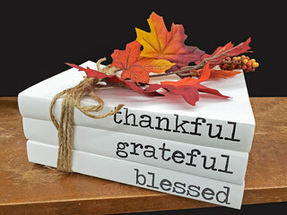 stack of books with text on white dust covers and fall leaves tied with rope string