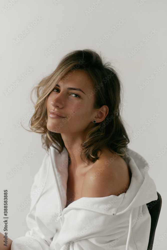Portrait of beautiful young woman with brown hair and clean bronze skin without makeup on white background. Natural and healthy look. Neutral interior. Soft light. Portrait of beautiful young woman with brown hair and clean bronze skin without makeup on white background. Natural and healthy look. Neutral interior. Soft light.