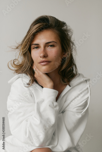 Portrait of beautiful young woman with brown hair and clean bronze skin without makeup on white background. Natural and healthy look. Neutral interior. Soft light. 