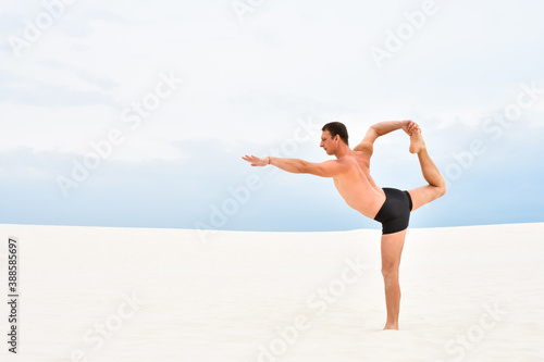 Young man in yoga pose natarajasana on the beach