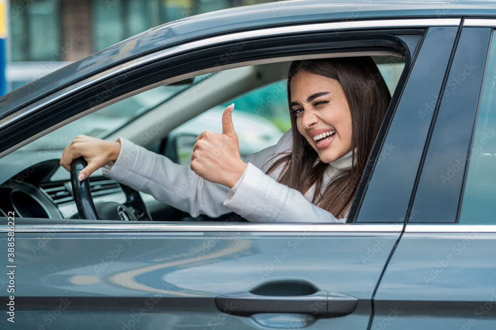 Young woman successfully passed a driving school test, happy face winking at camera holding thumb up