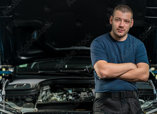 A car mechanic portrait in a front of the car under maintenance, in a garage