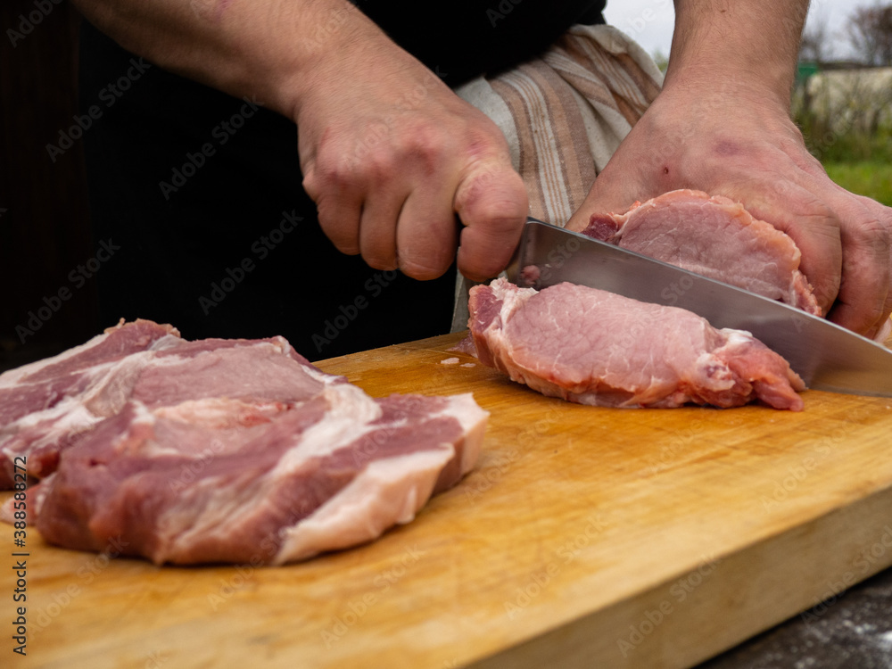 a man cuts meat steaks with a knife. pork loin without bones. cook in a black apron with a towel on his side.