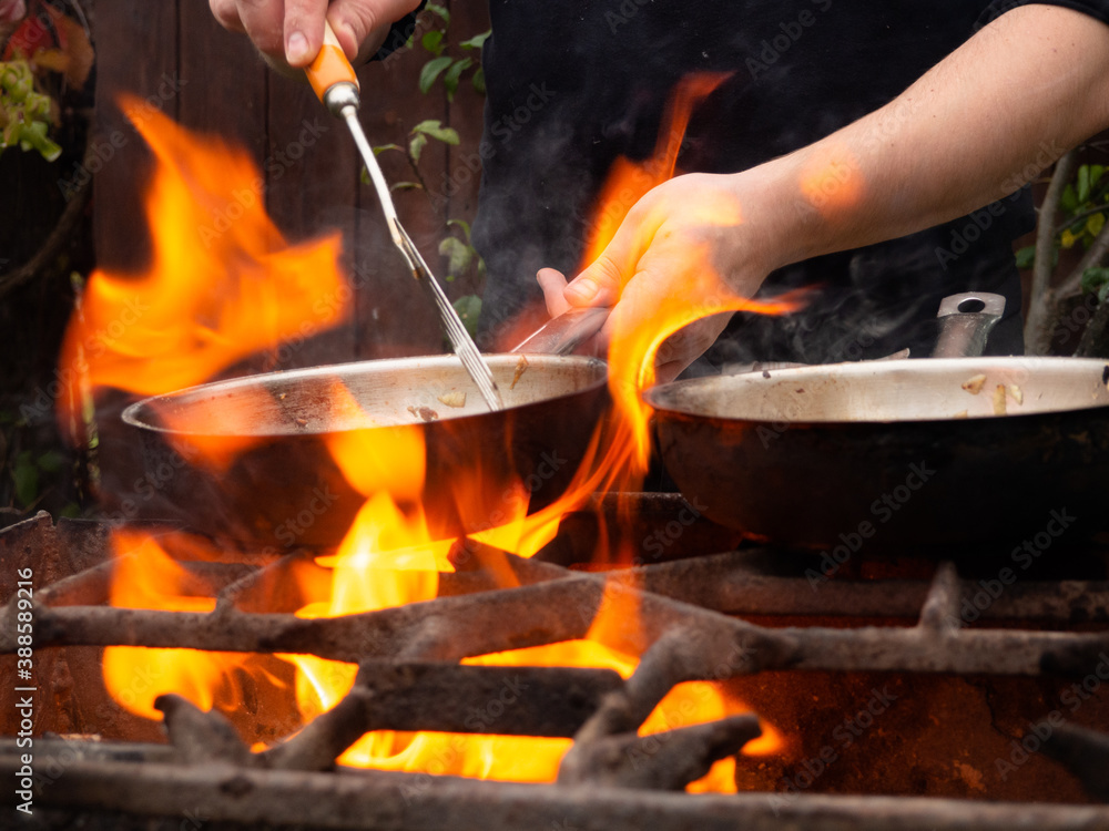 cooking on the grill in a frying pan. frying pan on fire. a man stirs food in a frying pan cooking on the grill in a frying pan. frying pan on fire. a man stirs food in a frying pan