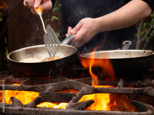 cooking on the grill in a frying pan. frying pan on fire. a man stirs food in a frying pan