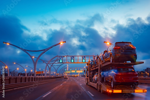 Car transporter with passenger cars. An auto transporter drives along an empty road. Cargo truck transports cars. Car transporter drives through the evening city