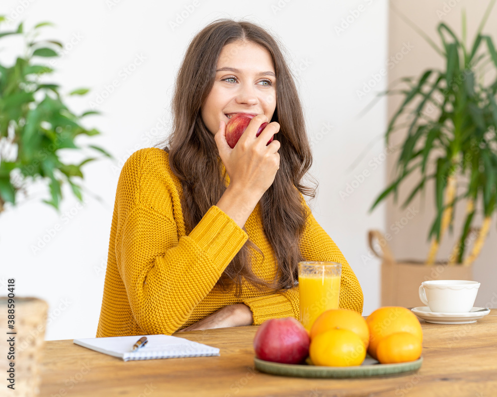 Young girl bitting red apple, smiling. Beautiful woman with long hair in bright yellow sweater eating fruits for detox Young girl bitting red apple, smiling. Beautiful woman with long hair in bright yellow sweater eating fruits for detox