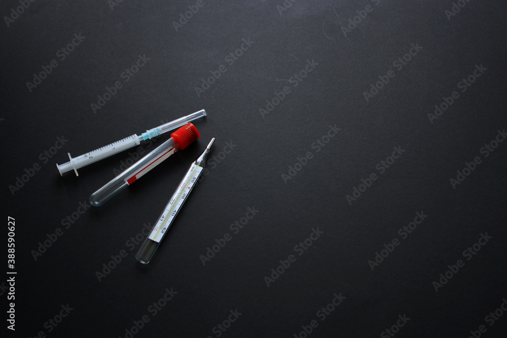 Medical equipments intended for diagnostic and treatment of the coronavirus infection (COVID-19) on a black background. Thermometer, vacutainer (test tube) and syringe. Medical equipments intended for diagnostic and treatment of the coronavirus infection (COVID-19) on a black background. Thermometer, vacutainer (test tube) and syringe.