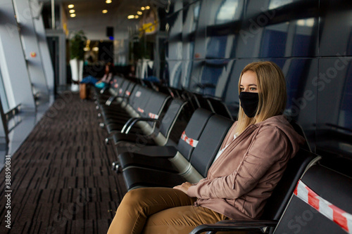 Woman tourist with a mask on her mouth protects against the virus. She sitting with a distance and waiting her plane. 
