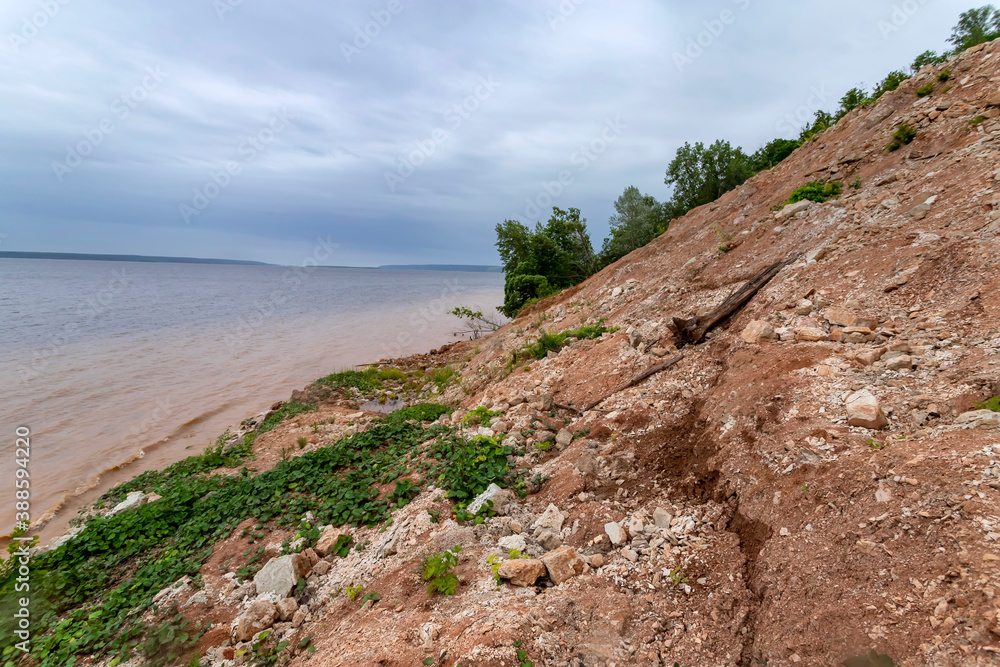 High bank of red clay and muddy water of the Volga river bay on a cloudy day. High bank of red clay and muddy water of the Volga river bay on a cloudy day.