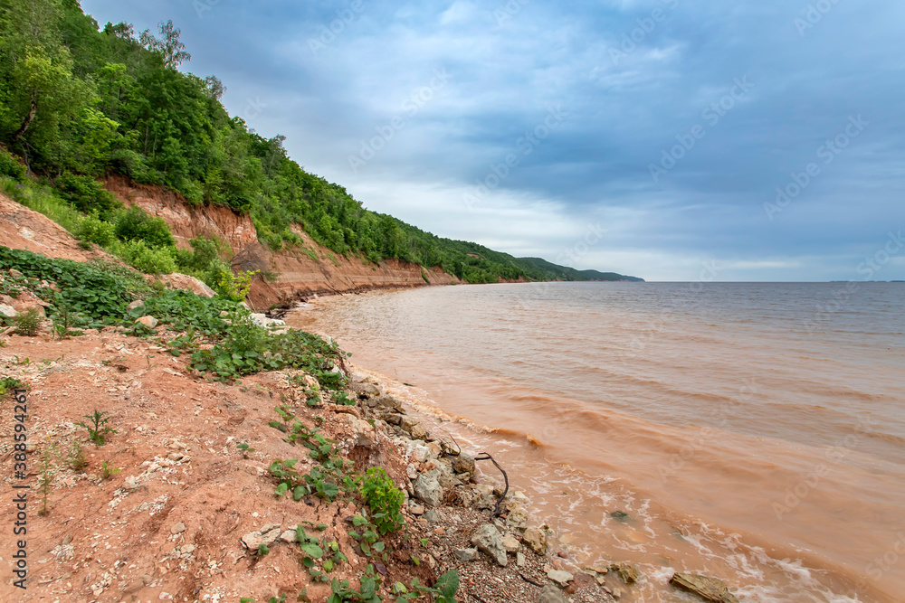 High bank of red clay and muddy water of the Volga river bay on a cloudy day.