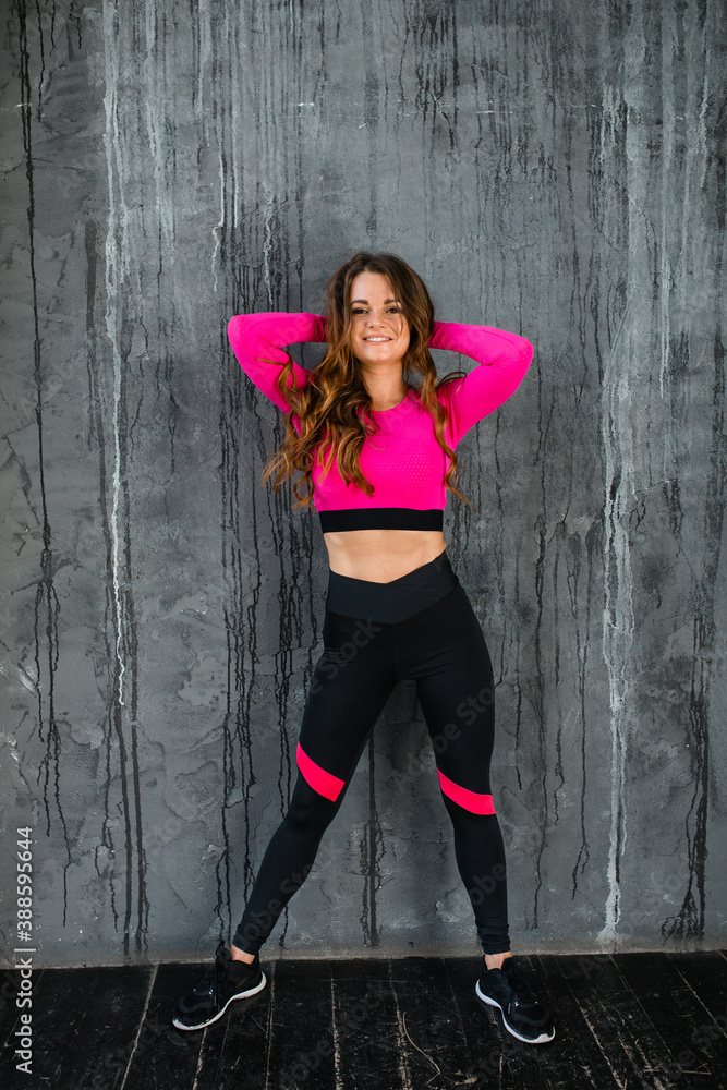 Fototapeta premium Beautiful attractive girl in bright sportswear in a loft studio on a background of a gray wall. Warm up, sports, healthy lifestyle